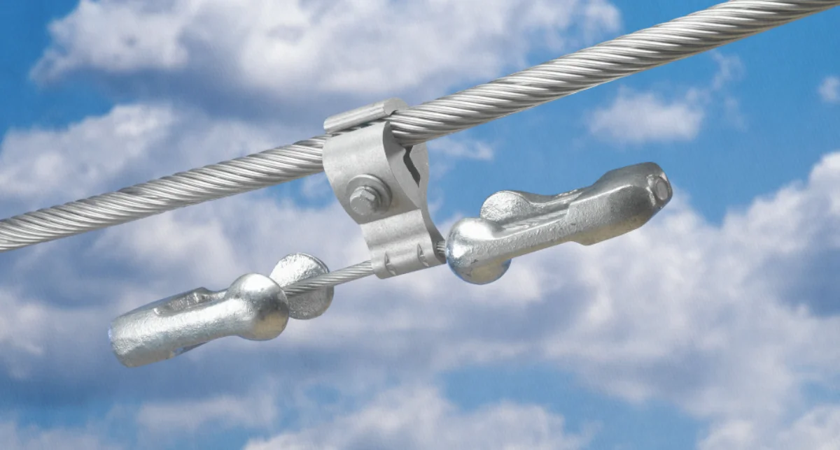 Stockbridge dampers are securely attached to a large overhead power line, visible against a blue sky with scattered clouds